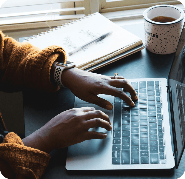 Person typing on a laptop at a desk with a notebook and coffee mug, describing a home service request